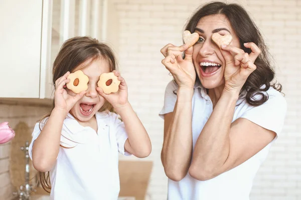 Happy mother and daughter with tasty cookies having fun in kitchen at home — Stock Photo, Image