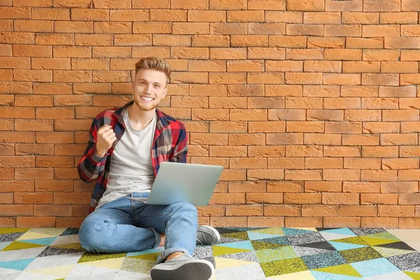 Happy young man with laptop sitting near brick wall — Stock Photo, Image