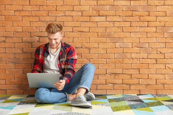 Handsome young man with laptop sitting near brick wall — Stock Photo, Image