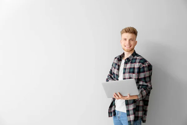 Handsome young man with laptop on light background — Stock Photo, Image