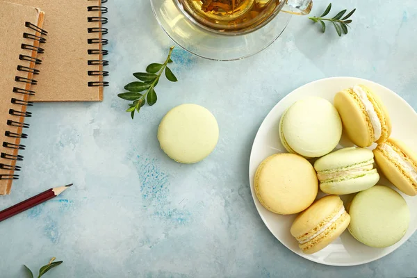 Tasty macarons with cup of tea and stationery on color background — Stock Photo, Image