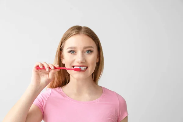 Beautiful woman cleaning teeth on light background — Stock Photo, Image