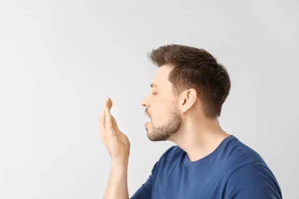 Man checking freshness of his breath on light background — Stock Photo, Image