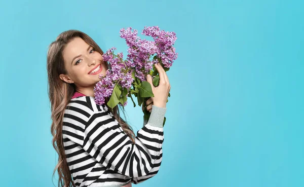 Krásná mladá žena s kyticí fialovými květy na barevném pozadí — Stock fotografie