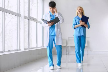 Erkek doktor ve kadın tıbbi asistan klinikte koridorda yürüyor