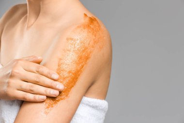 Güzel genç kadın gri arka plan karşı vücut scrub uygulayarak, closeup