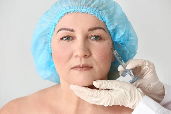 Mature woman receiving injection in face on light background — Stock Photo, Image