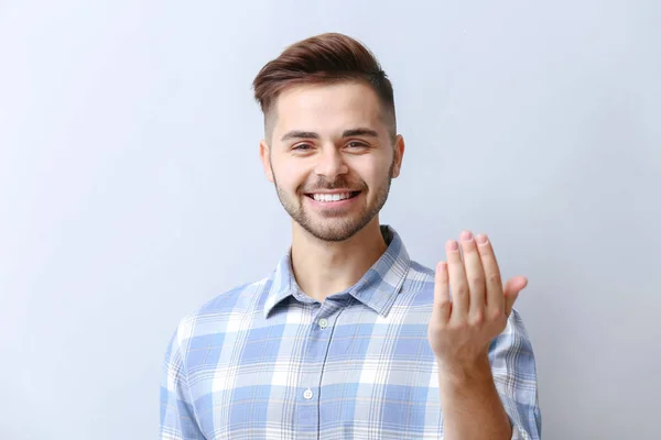 Knappe man toont "kom hier" gebaar op lichte achtergrond — Stockfoto