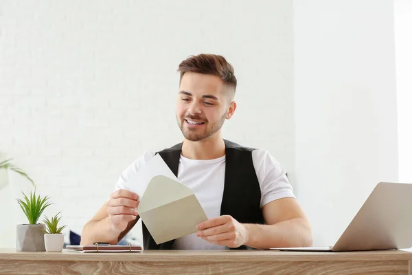 Young man opening envelope with invitation at home — Stock Photo, Image