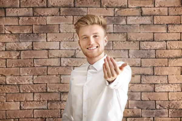 Handsome young man inviting viewer against brick background — Stock Photo, Image