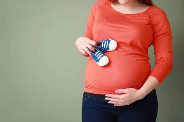 色の背景に赤ちゃんのブーツを持つ美しい妊娠中の女性 — ストック写真