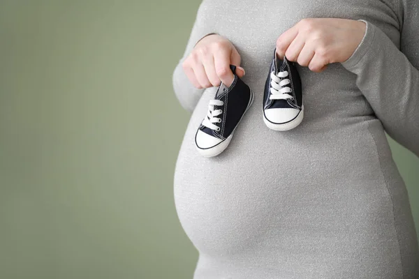 色の背景に赤ちゃんのブーツを持つ美しい妊娠中の女性、クローズアップ — ストック写真