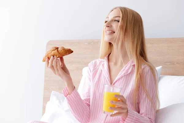 Güzel genç bir kadın yatakta kahvaltı yapıyor. — Stok fotoğraf