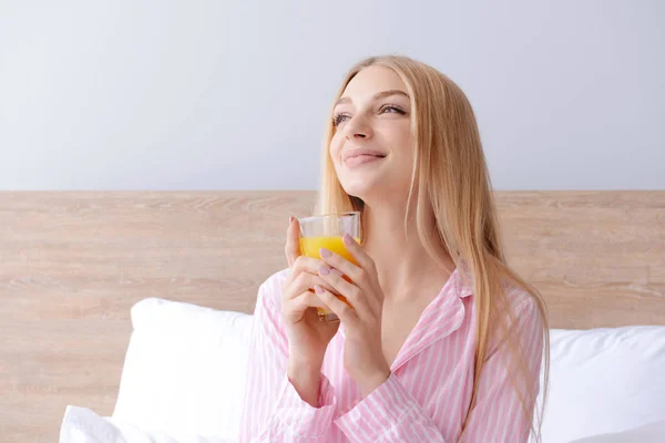 Beautiful young woman drinking fresh juice in bed — Stock Photo, Image