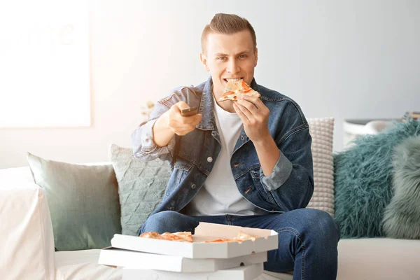 Handsome man eating tasty pizza while watching TV at home — Stock Photo, Image