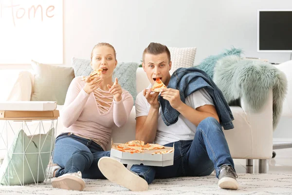 Young couple eating tasty pizza while watching TV at home — Stock Photo, Image