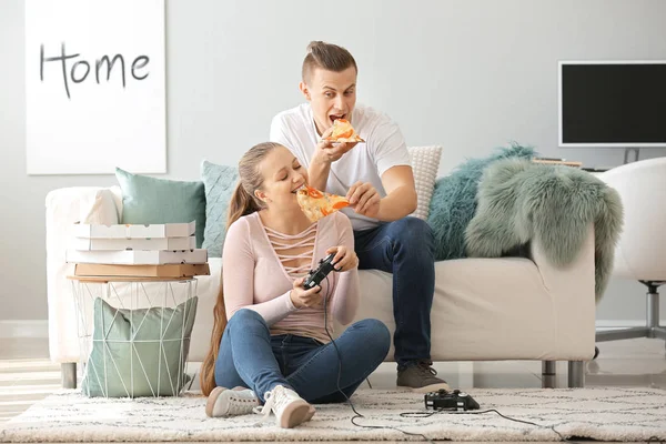 Young couple eating tasty pizza while playing video games at home — 스톡 사진