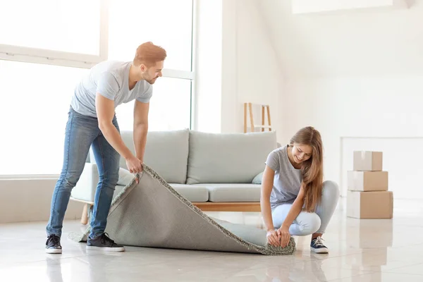 Young couple unrolling carpet on floor — Stock Photo, Image