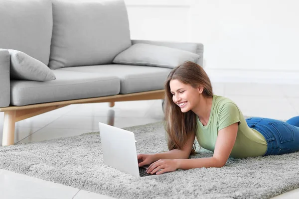 Jonge vrouw met laptop liggend op zacht tapijt thuis — Stockfoto