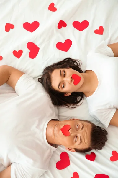 Glückliches junges Paar mit Papierherzen im Bett liegend — Stockfoto