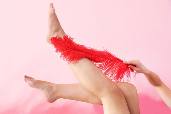 Hermosa mujer joven con plumas en sus piernas contra el fondo de color. Concepto de depilación — Foto de Stock