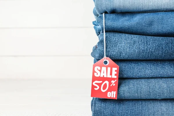 Stack of different jeans pants with shopping tag on white background — Stock Photo, Image