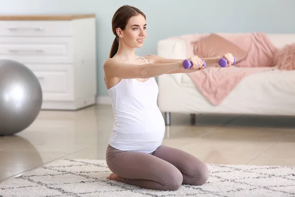 Mulher grávida bonita com halteres formação em casa — Fotografia de Stock