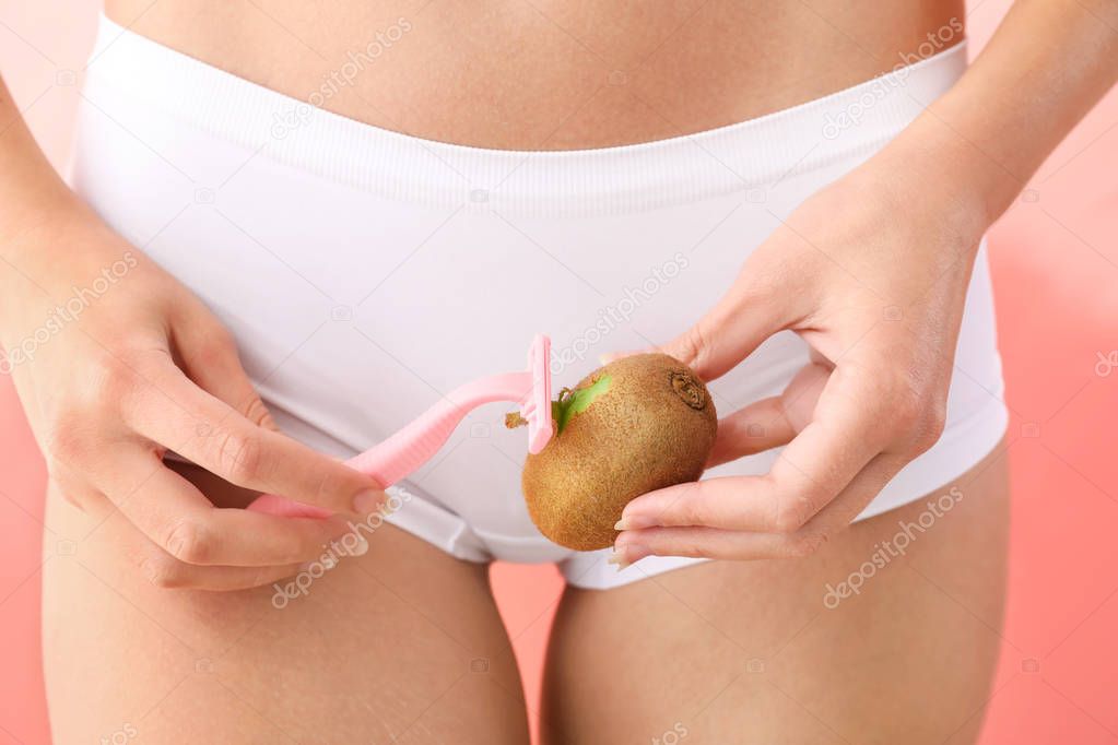 Beautiful young woman shaving kiwi on color background, closeup. Depilation concept