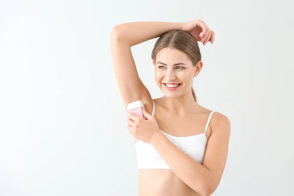 Beautiful young woman epilating armpits on light background — Stock Photo, Image