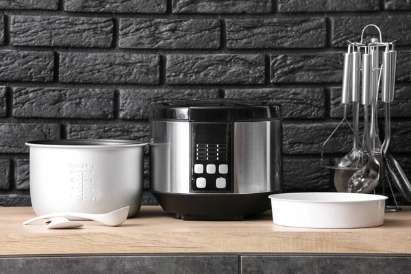 Modern multi cooker with accessories on table against dark background — Stock Photo, Image