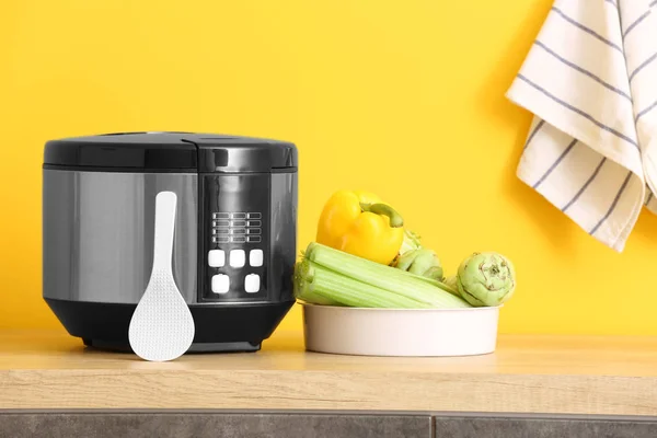 Modern multi cooker with vegetables on table against color background — Stock Photo, Image