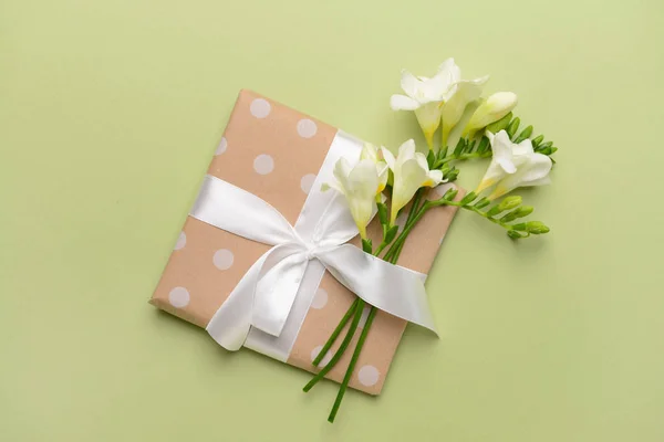 Beautiful freesia flowers and gift on color background — Stock Photo, Image