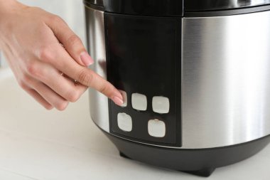 Woman switching on modern multi cooker on table, closeup