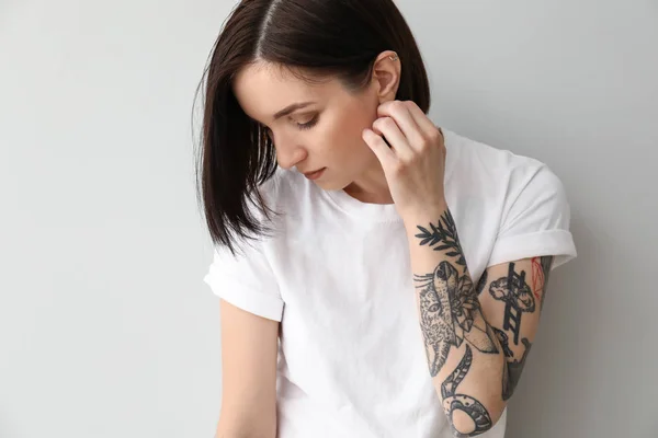 Stylish tattooed woman on light background — Stock Photo, Image
