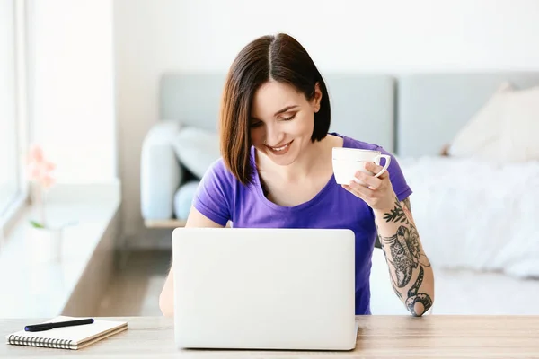 Belle femme tatouée buvant du café et travaillant sur un ordinateur portable à la maison — Photo