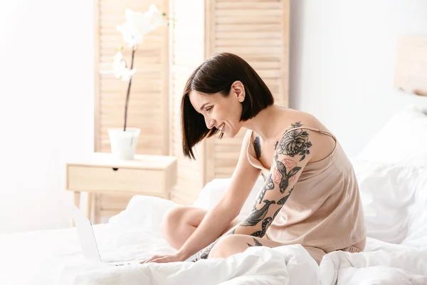 Morning of beautiful tattooed woman with laptop in bedroom — Stock Photo, Image