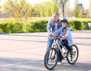 Baba oğluna dışarıda bisiklete binmeyi öğretiyor.