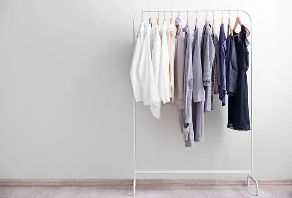 Rack with stylish clothes near light wall — Stock Photo, Image