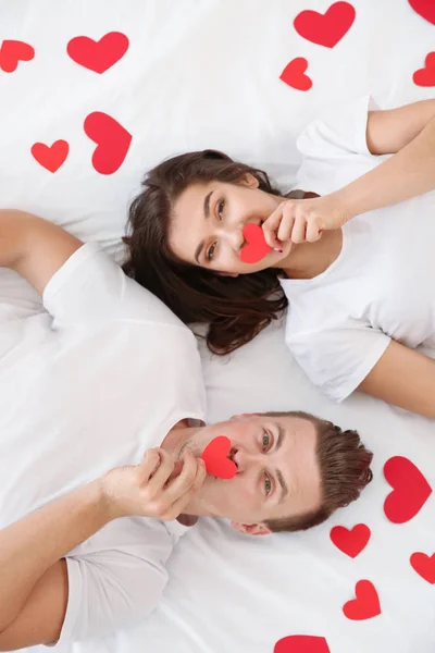Jovem casal feliz com corações de papel deitado na cama — Fotografia de Stock