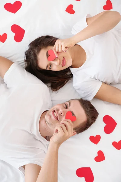 Jovem casal feliz com corações de papel deitado na cama — Fotografia de Stock