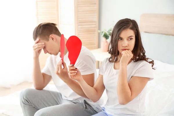 Pareja joven infeliz con el corazón de papel roto en el dormitorio. Conflicto en la relación —  Fotos de Stock