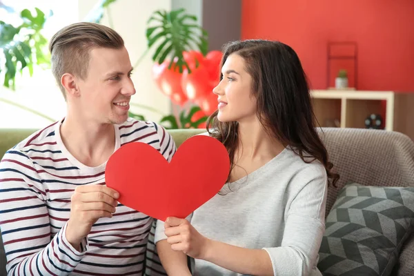 Happy young couple with paper heart at home — Stock Photo, Image