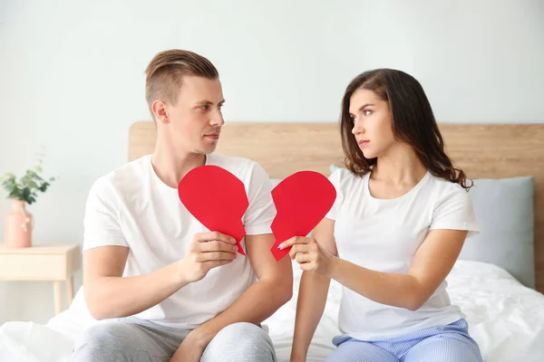 Casal jovem infeliz com coração de papel rasgado no quarto. Conflito na relação — Fotografia de Stock