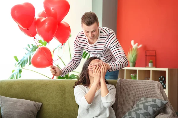 Jovem cumprimentando com balões de ar em forma de coração sua esposa em casa — Fotografia de Stock