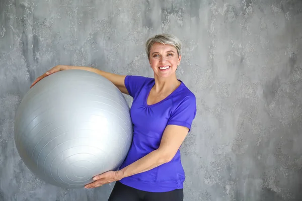 Sporty donna matura con fitball su sfondo grigio — Foto Stock
