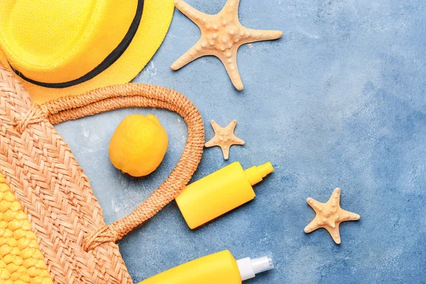 Beach bag with sun protection cream, lemon fruit and starfishes on color background — Stock Photo, Image