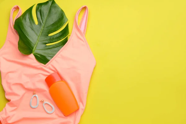 Sonnenschutzcreme mit weiblichem Badeanzug und Ohrringen auf farbigem Hintergrund — Stockfoto