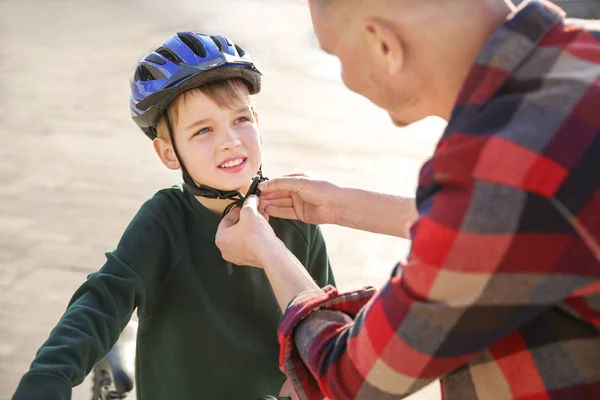 Father helping his son to put on bicycle helmet outdoors — Stock Photo, Image