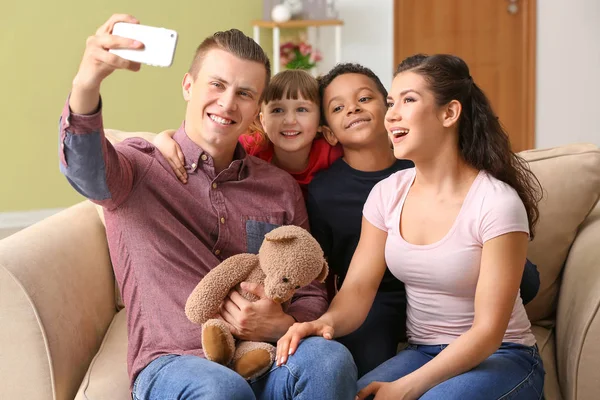 Happy couple with little adopted children taking selfie at home — Stock Photo, Image