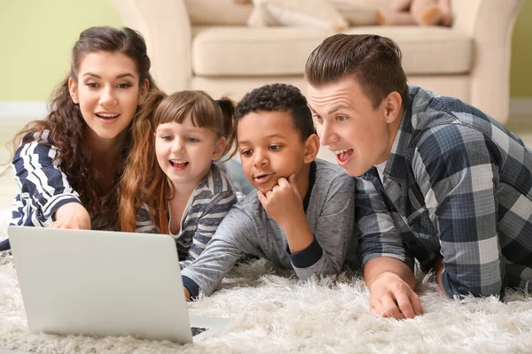 Glückliches Paar mit kleinen Adoptivkindern mit Laptop zu Hause — Stockfoto